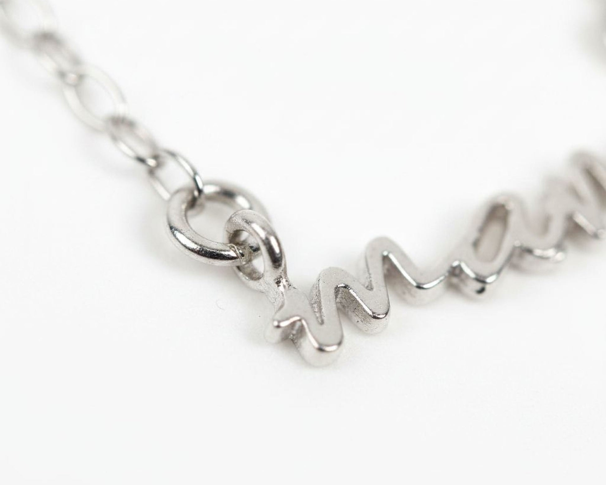 A close-up view of a silver necklace with the word "MOM" engraved on it.