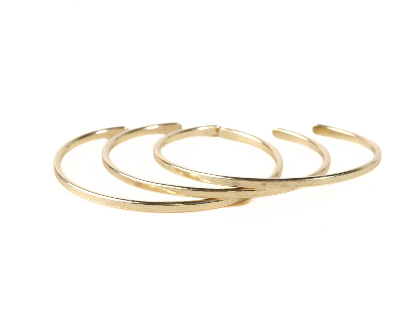 Three gold-colored bracelets are arranged in a circular pattern against a white background.