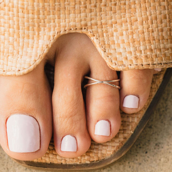 A close-up view of a person's foot wearing a woven straw sandal, with the toes and toenails painted in a light color.
