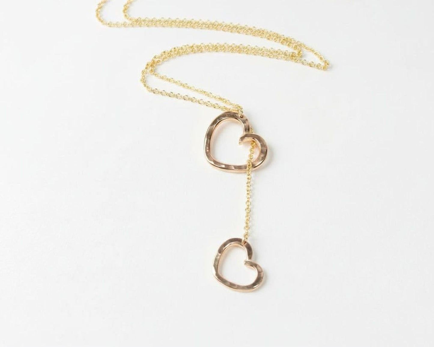 A delicate gold necklace with two heart-shaped pendants hanging from the chain.