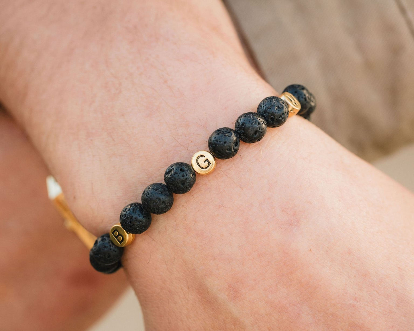 A bracelet made of black beads with gold letters on them, worn on a person's wrist.