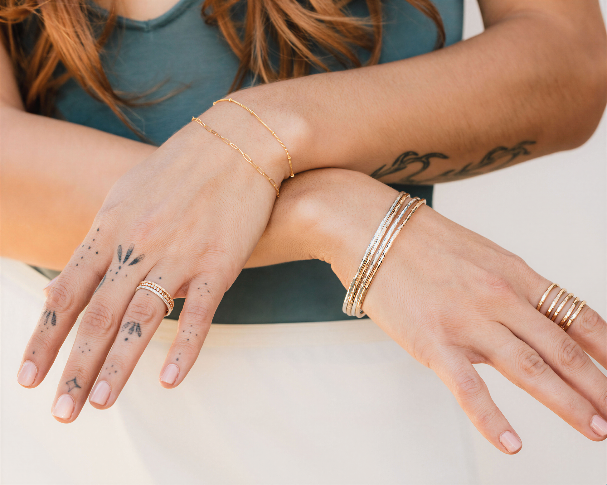 A close-up of a person's hands wearing multiple rings and bracelets, with tattoos visible on their fingers.