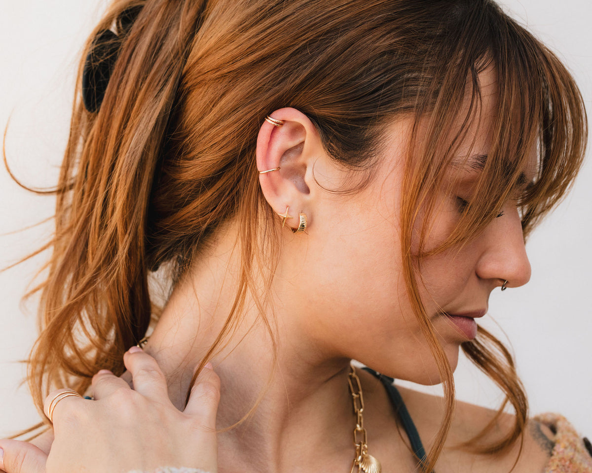 A close-up of a woman's face, with her hair styled in a ponytail and wearing multiple earrings.