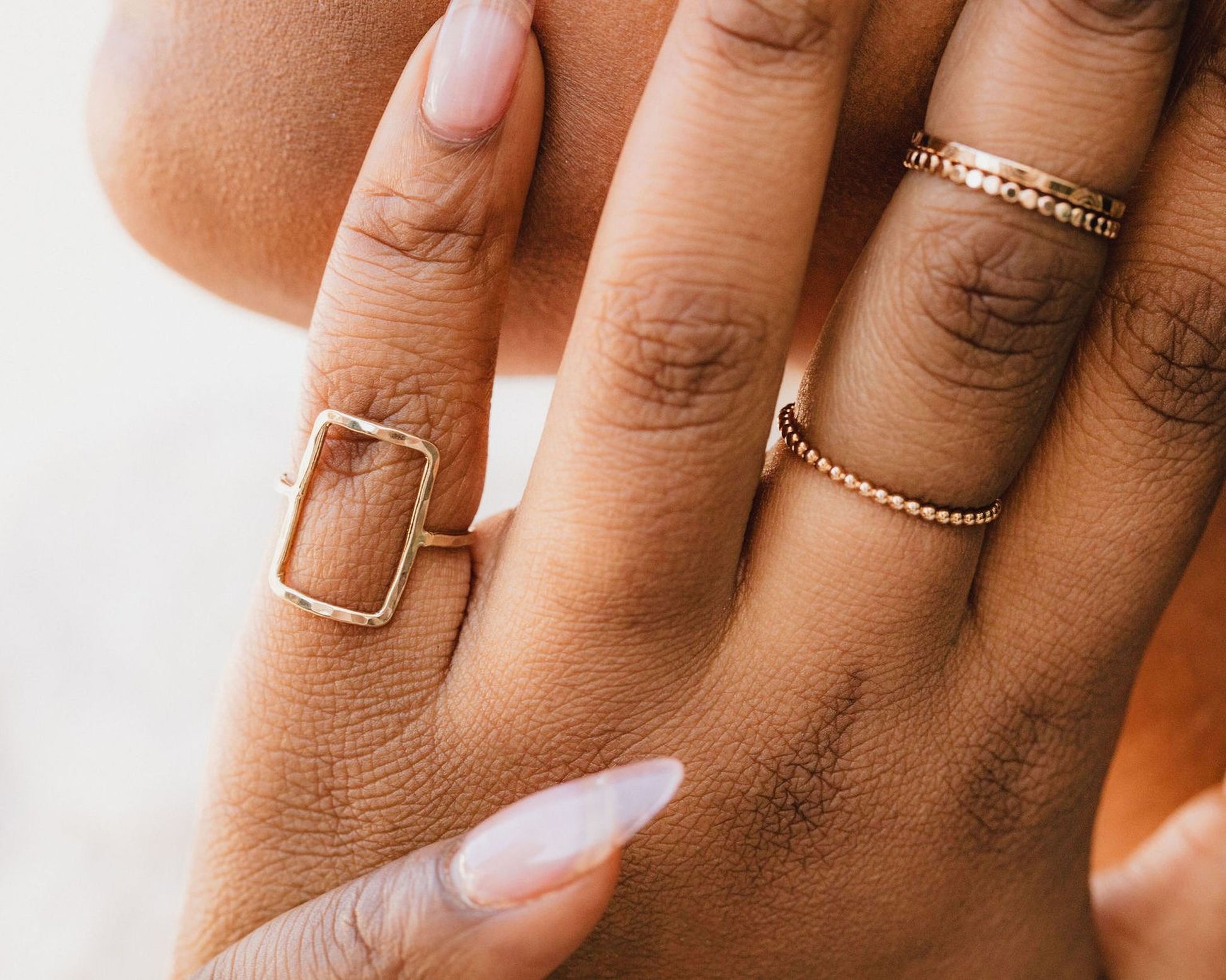 A close-up of a person's hand wearing multiple rings, including a rectangular ring and a ring with small beads.
