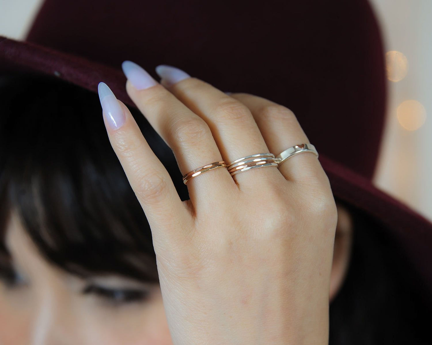 A close-up of a person's hand wearing multiple rings, with a burgundy hat partially obscuring the view.