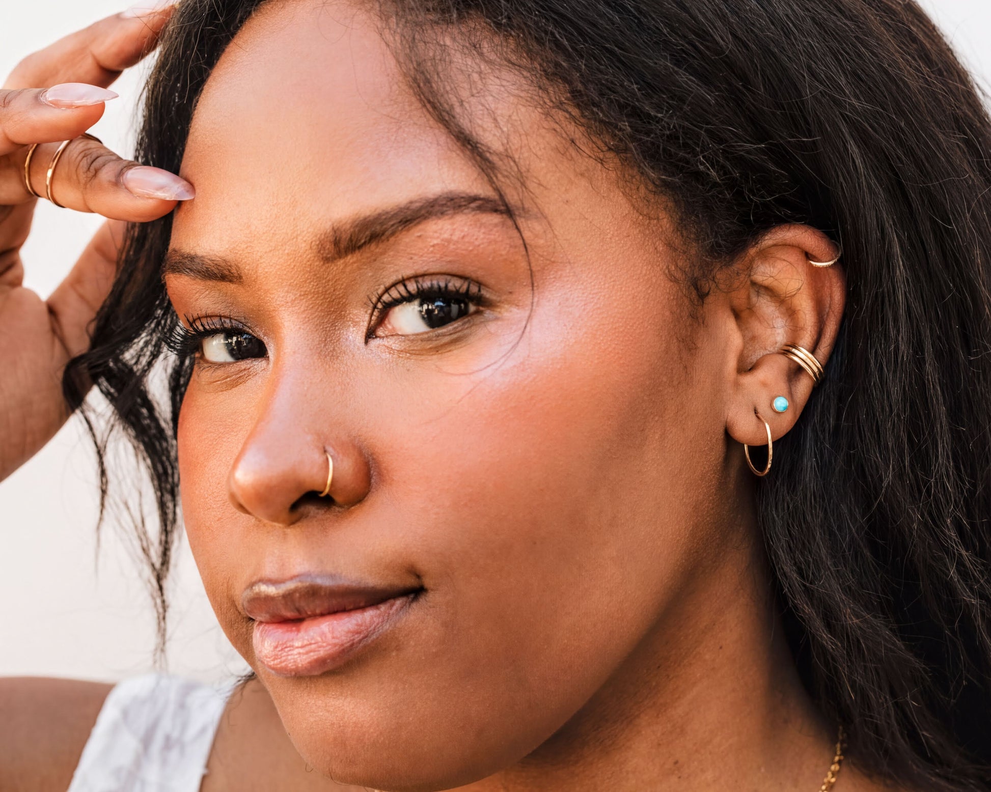 A close-up portrait of a woman with dark hair, wearing multiple rings and earrings, and looking directly at the camera with a neutral expression.