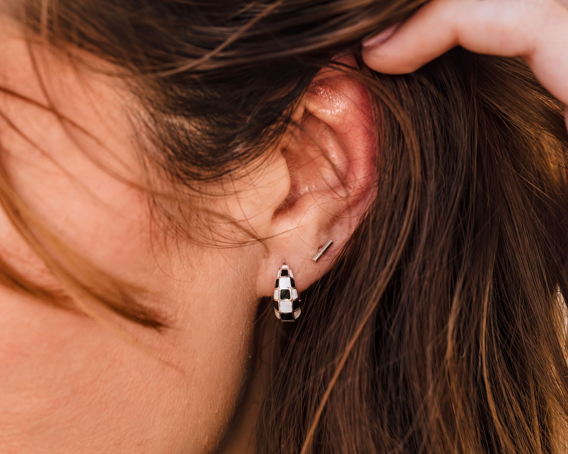 A close-up view of a person's ear with a pair of earrings, specifically a pair of hoop earrings with a checkered pattern.