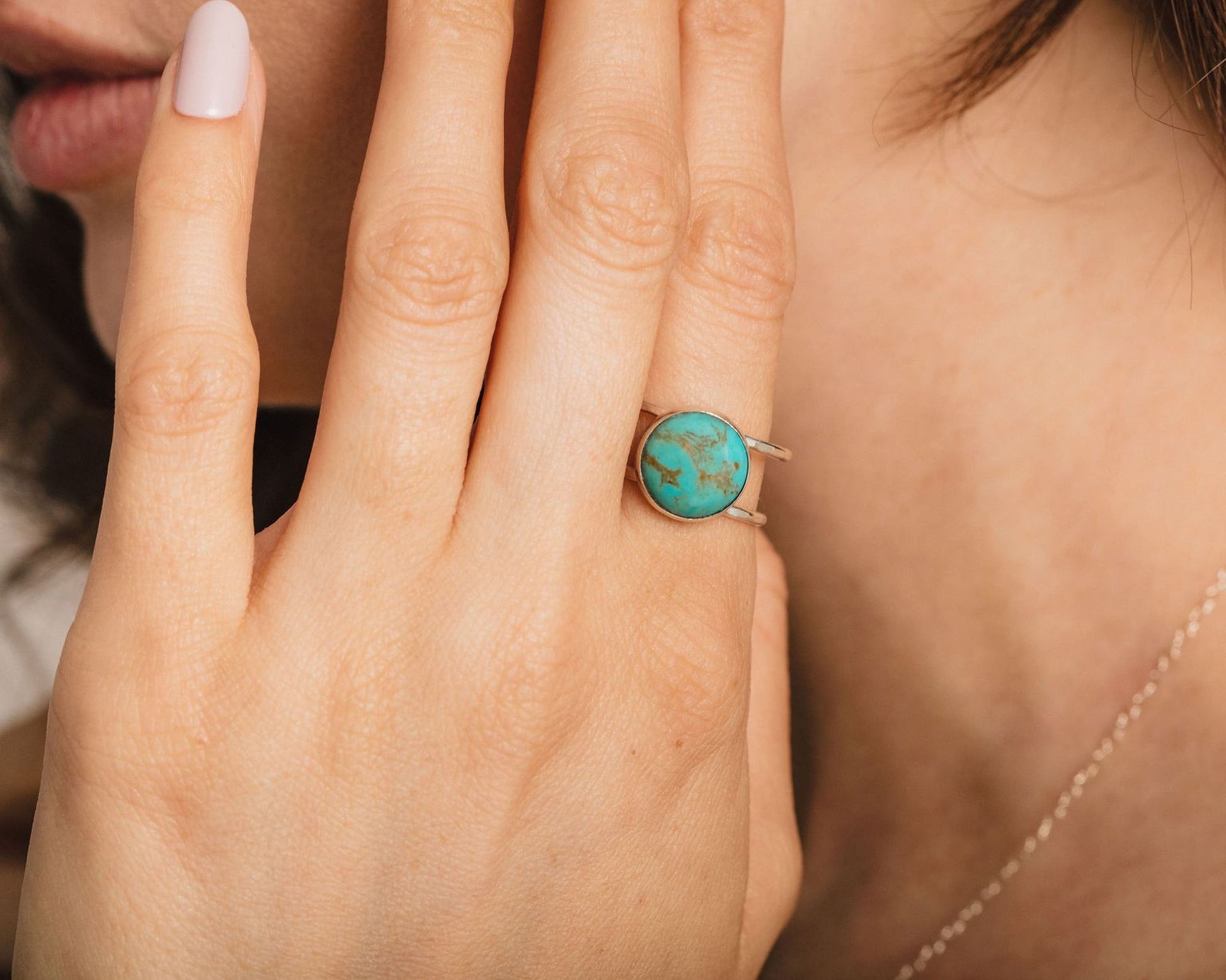 A close-up of a hand wearing a turquoise stone ring, with a person's face partially visible in the background.