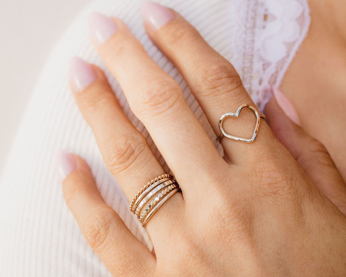 A close-up of a person's hand wearing multiple rings, including a heart-shaped ring and a ring with multiple tiers.
