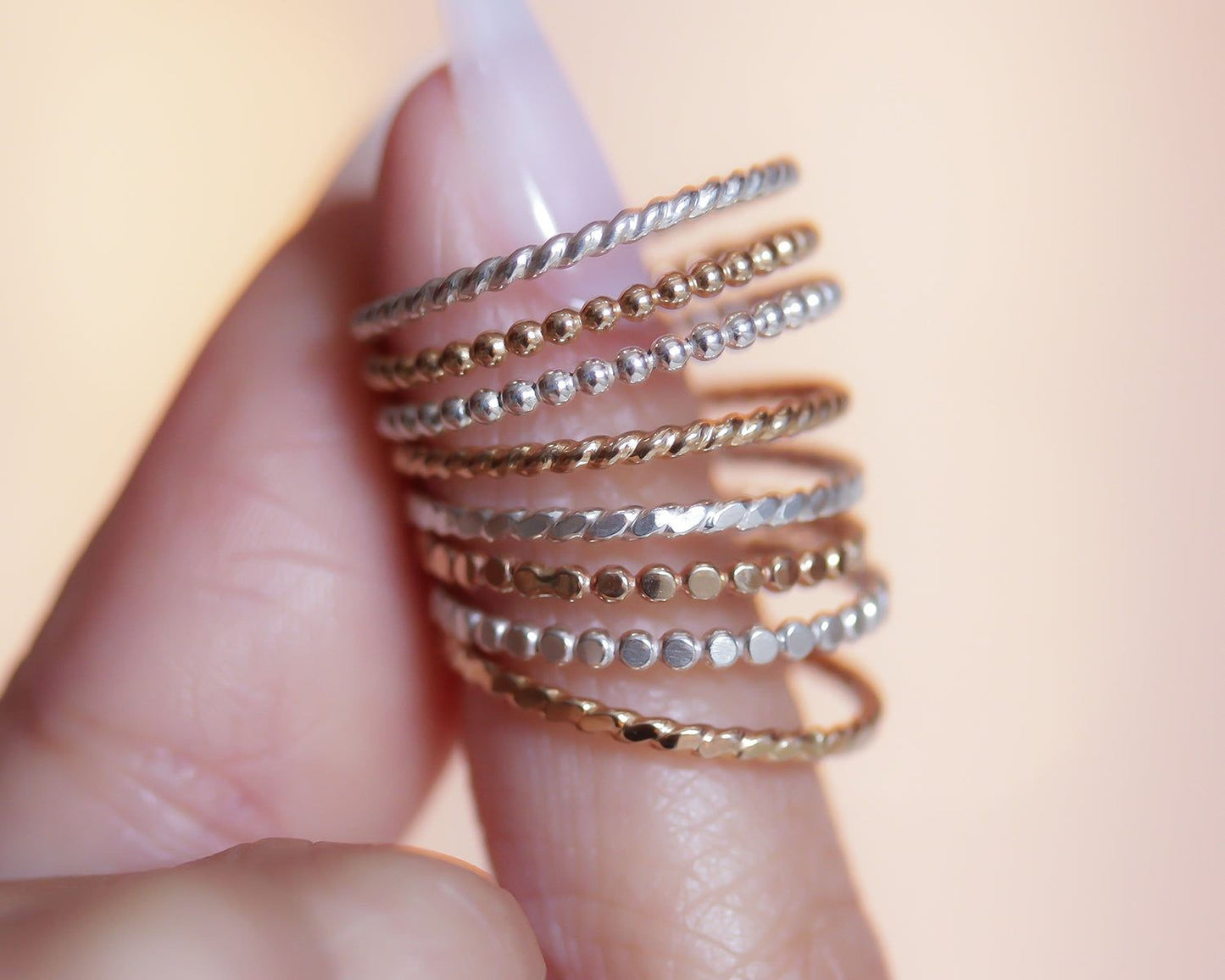 A hand holding a stack of rings on a finger, with the rings varying in size and design.