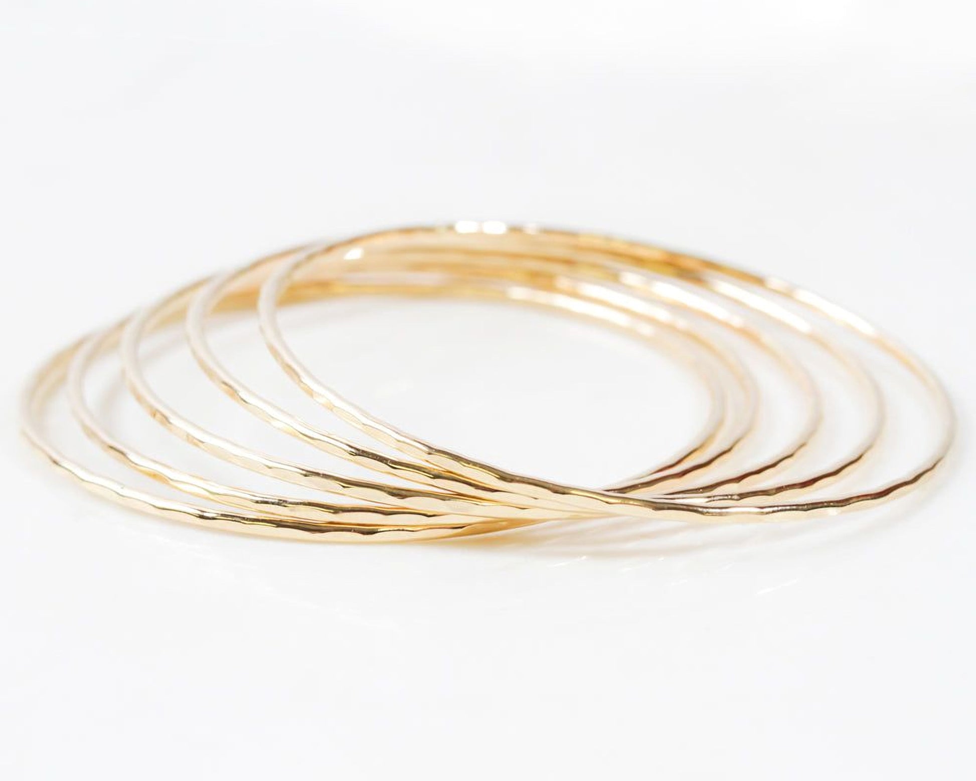 Image shows close up of the exquisite texture of our 14 karat yellow gold filled bangles. Showing five stunning bangles, each bracelet is hand hammered which gives them their special sparkle. Wear individually or stack them up to create a unique set.