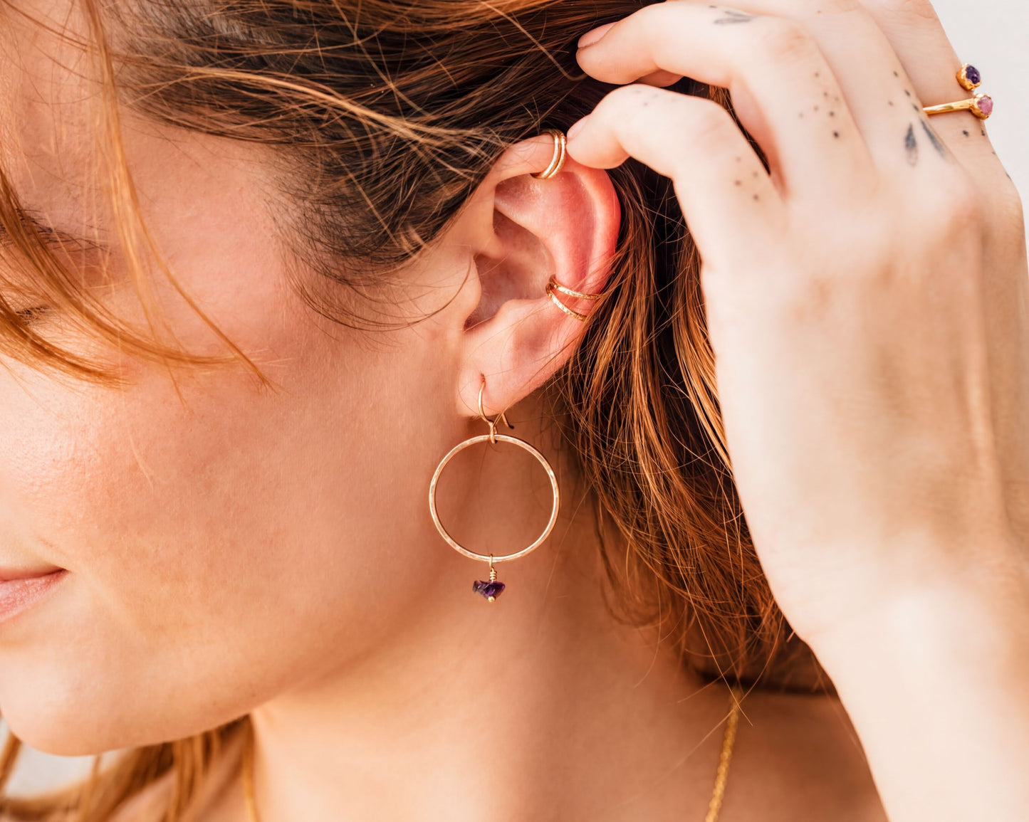 A close-up of a person's face, focusing on their ear and hand adorned with multiple rings and earrings.