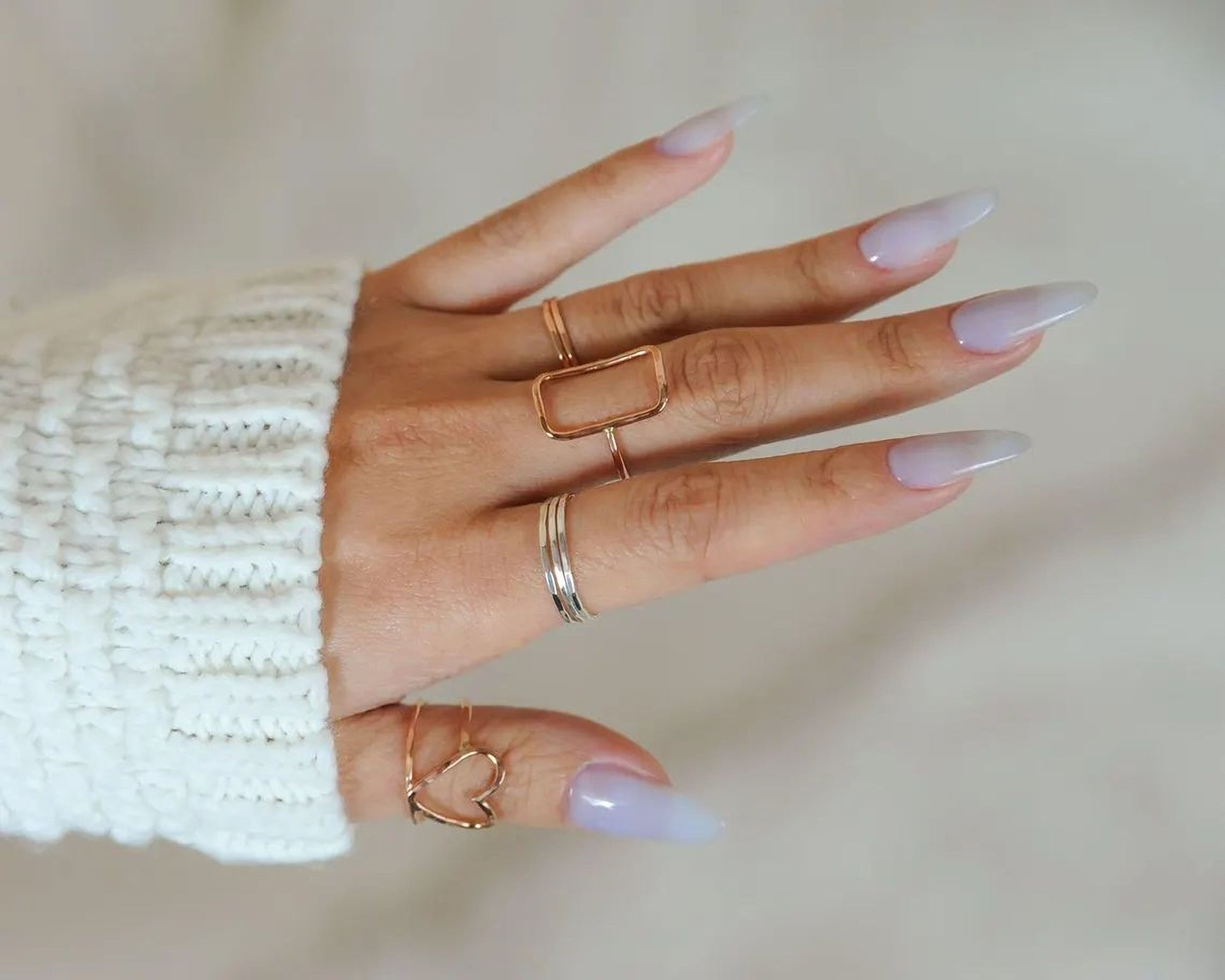 A close-up of a person's hand wearing multiple rings on their fingers, including a ring with a heart design.