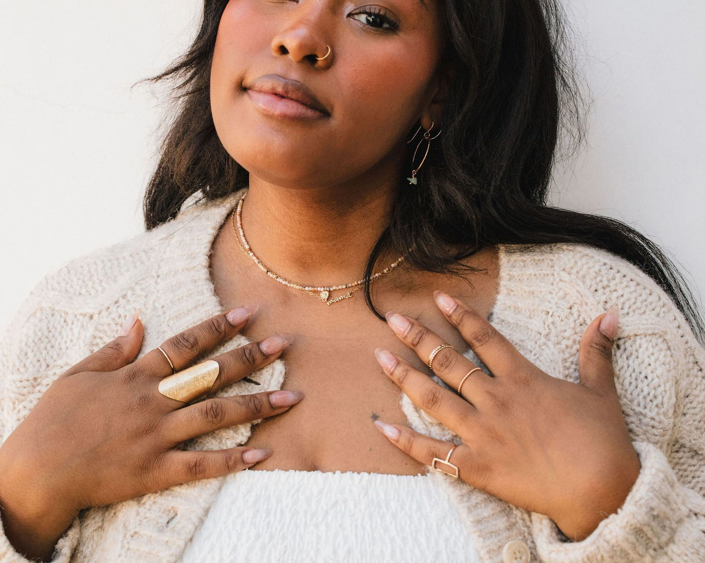A close-up of a woman wearing a white sweater and multiple rings on her fingers, with a neutral expression on her face.