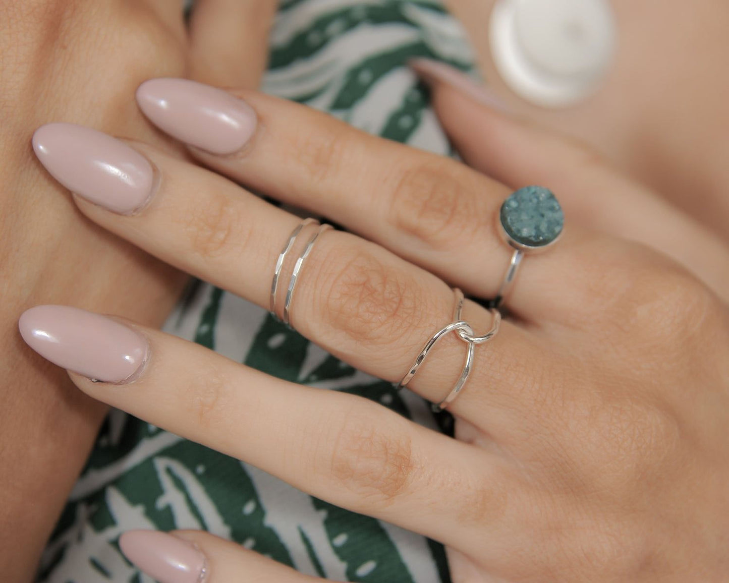 A close-up of a person's hand wearing multiple rings, including a ring with a blue stone and another ring with a silver band.