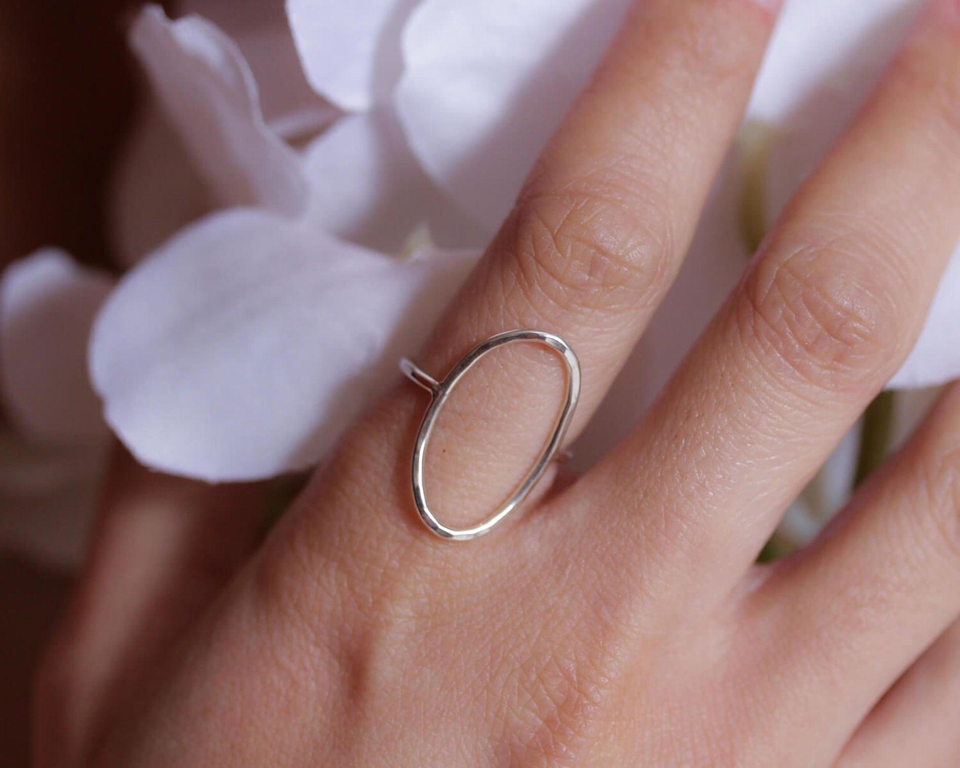 A close-up of a person's hand wearing a silver ring with an oval-shaped design.