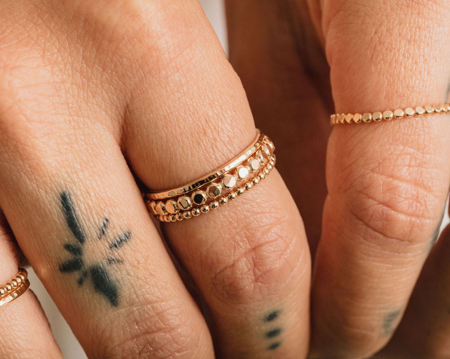 A close-up of a person's hand wearing multiple gold rings on the fingers, with a tattoo visible on the left hand.