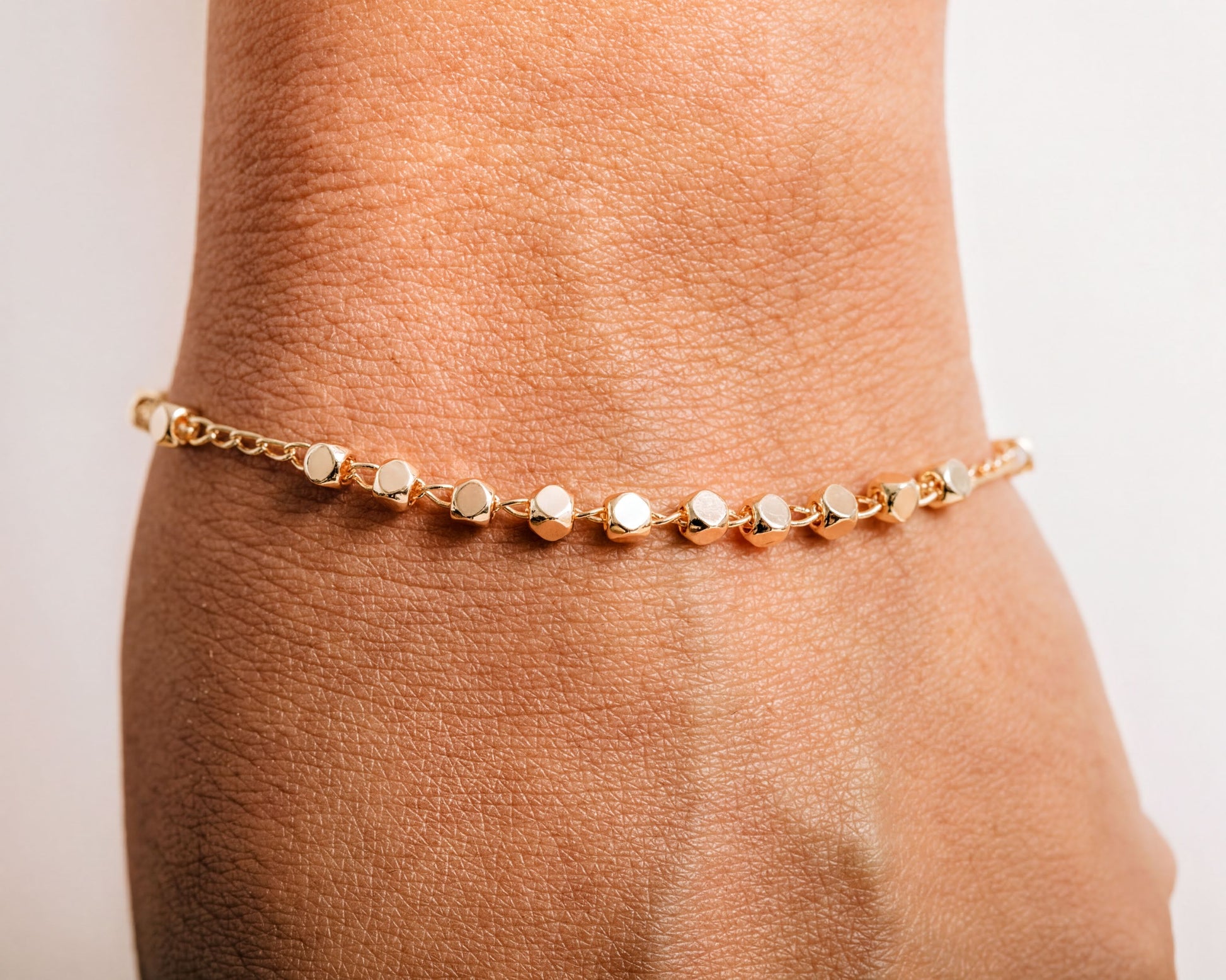 A gold-colored bracelet with small, round beads is worn on a person's wrist.