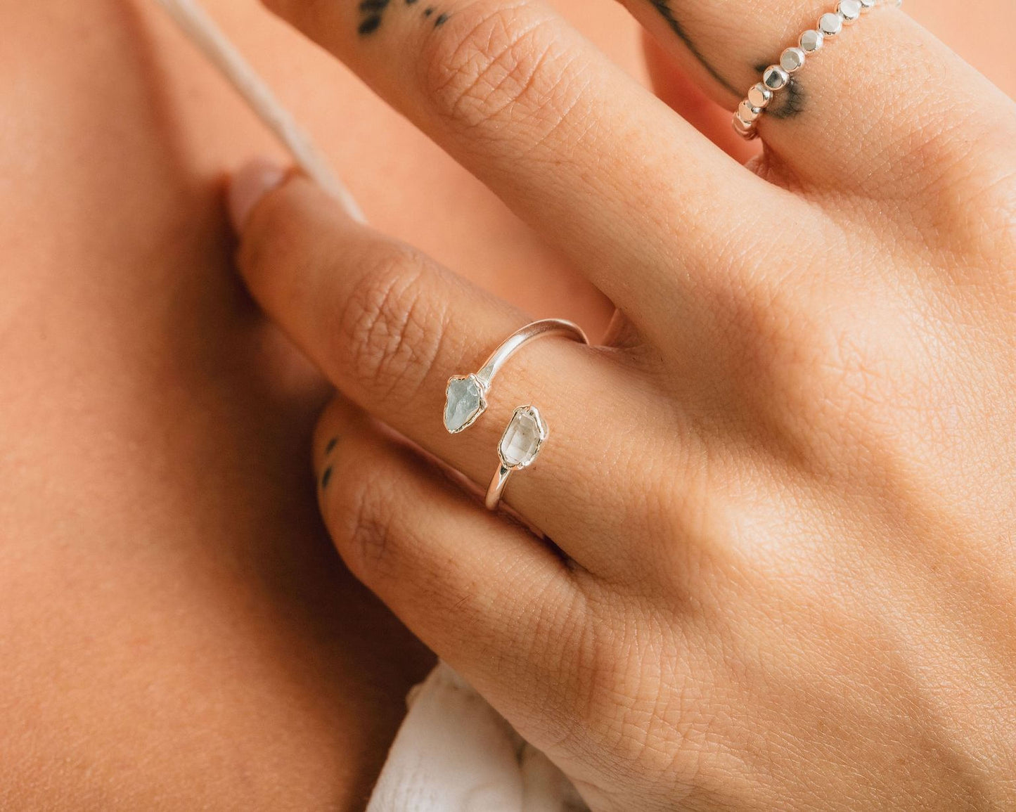 A close-up of a person's hand wearing a silver ring with two green gemstones.