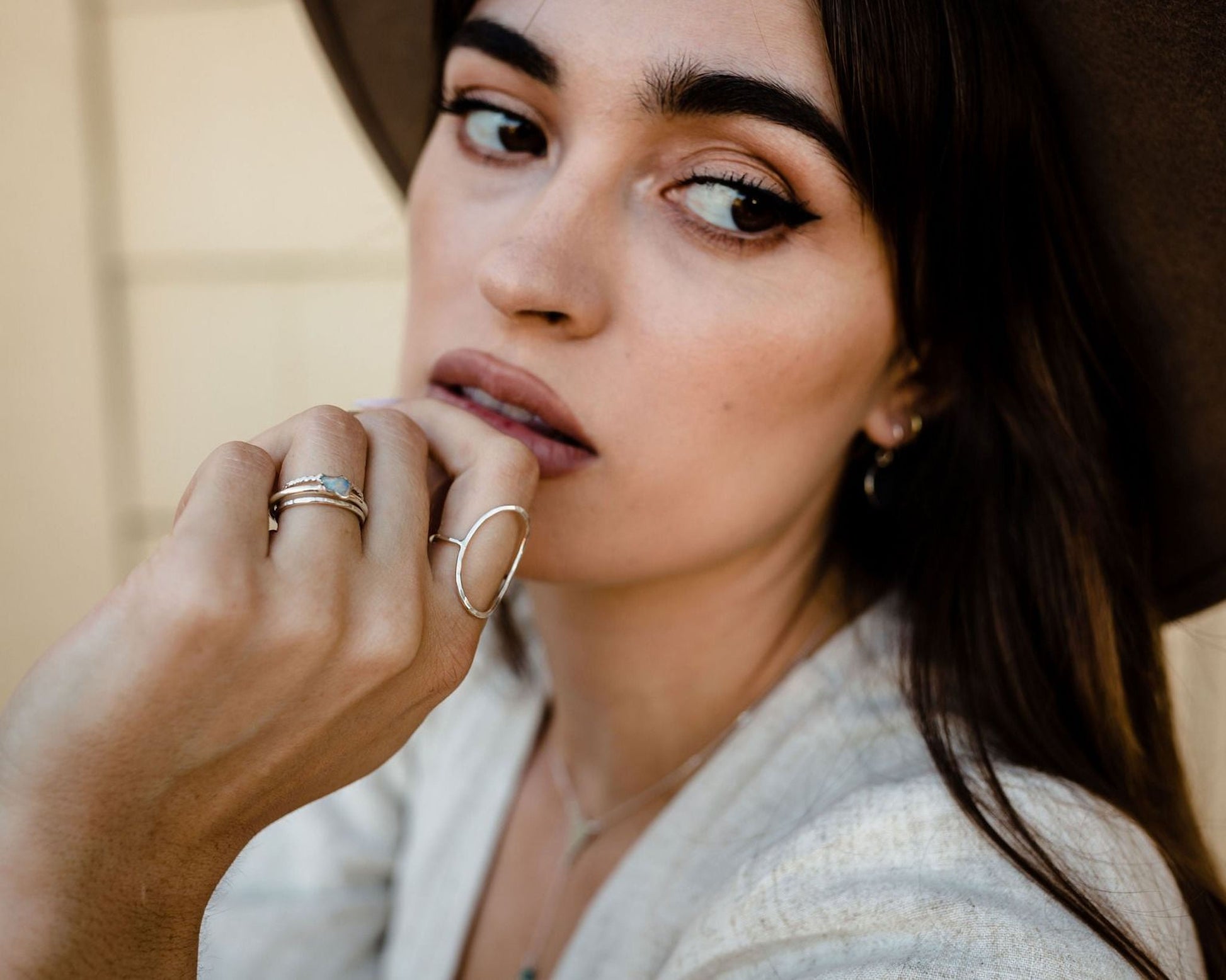 A close-up portrait of a woman with dark hair, wearing a hat and a white top. She is looking directly at the camera with a thoughtful expression.