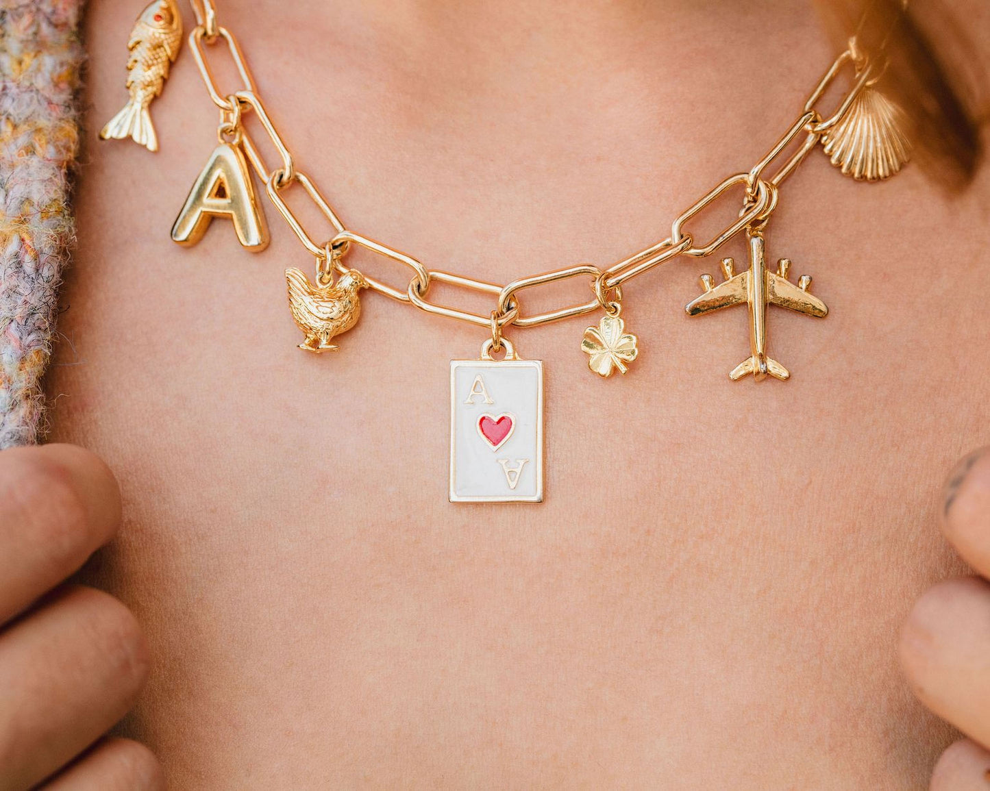 A close-up view of a person's neck adorned with a gold-colored necklace featuring various charms, including a heart-shaped charm, a letter 'A' charm, and a small airplane charm.