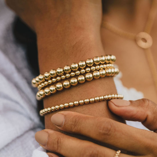 A close-up view of a person's wrist adorned with multiple gold-colored beaded bracelets.