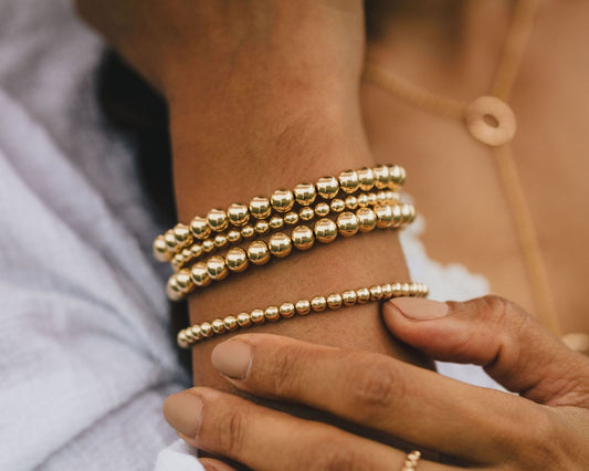 A close-up view of a person's wrist adorned with multiple gold-colored beaded bracelets.