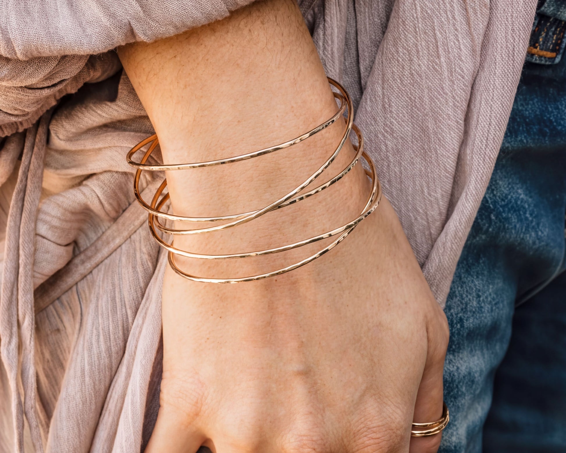A close-up view of a person's hand wearing multiple gold-colored bracelets on the wrist.