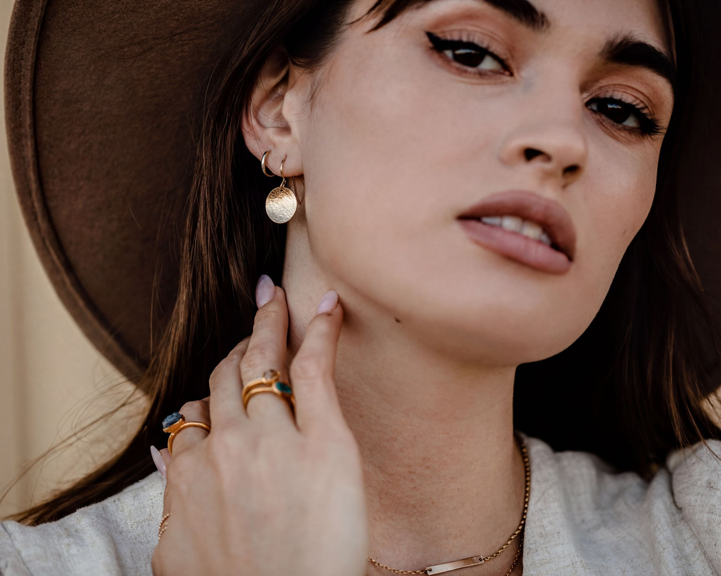A close-up portrait of a woman wearing a brown hat and multiple rings on her fingers, with a serious expression on her face.