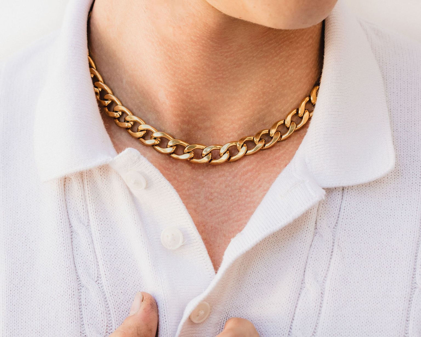A close-up of a person wearing a gold chain necklace and a white collared shirt.