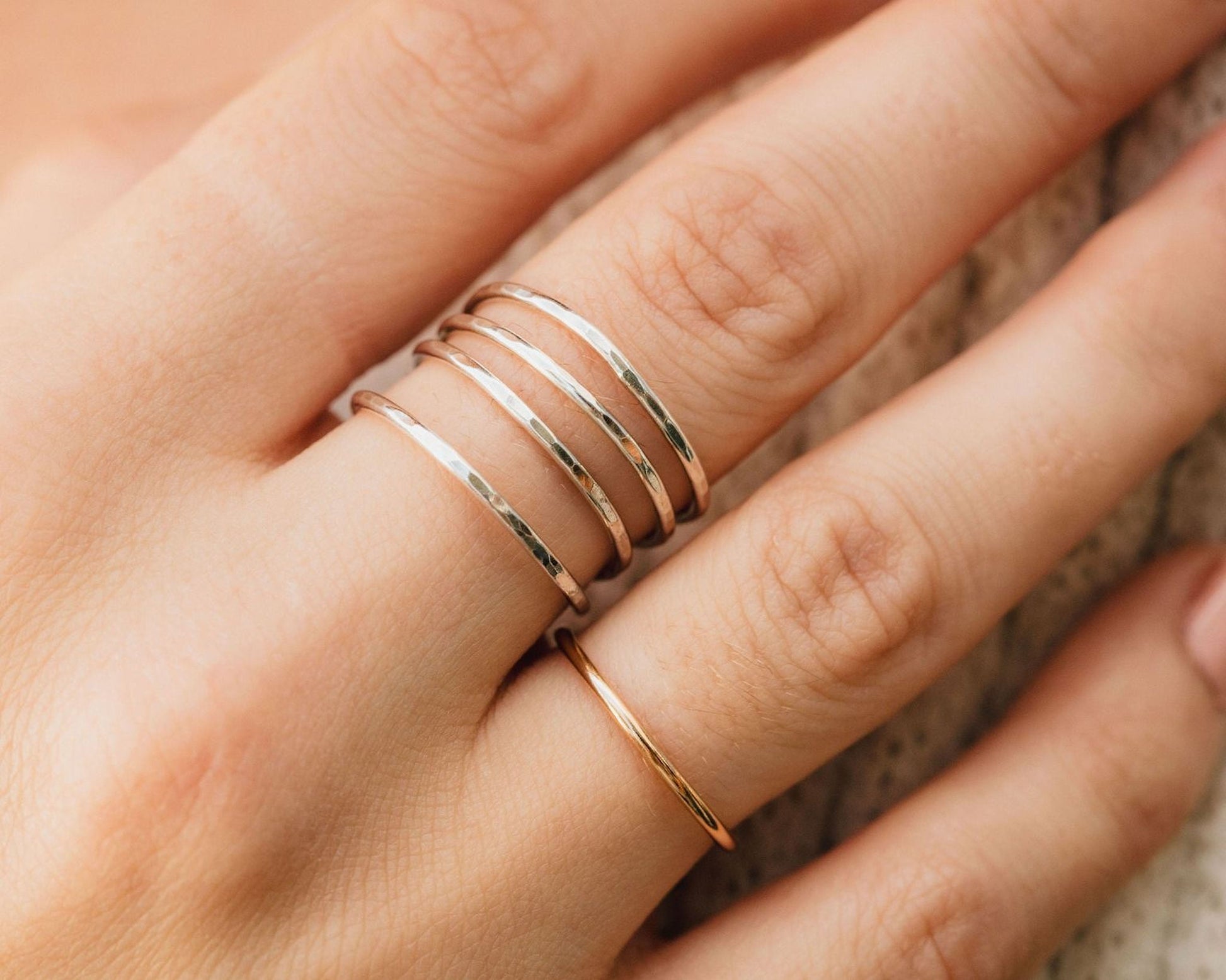 A close-up view of a person's hand wearing multiple rings on the fingers.