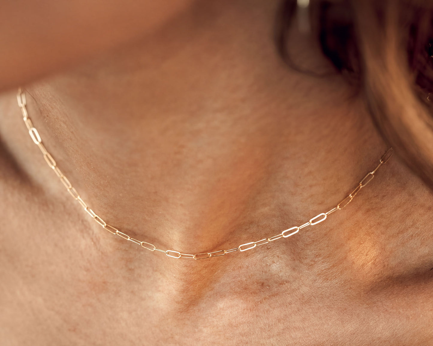 A close-up view of a delicate gold chain necklace worn around a person's neck.