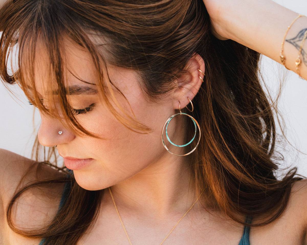 A close-up of a woman's face, with her eyes closed and her hair styled in loose waves. She is wearing large hoop earrings with turquoise and gold tones.