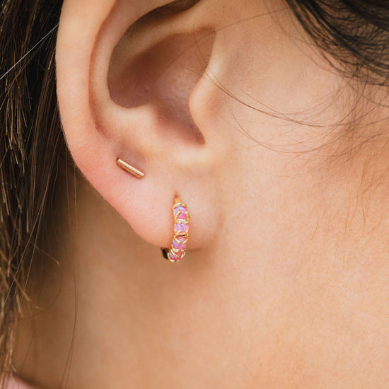 A close-up view of a person's ear adorned with two gold earrings, one of which is a small hoop earring with a pink gemstone.