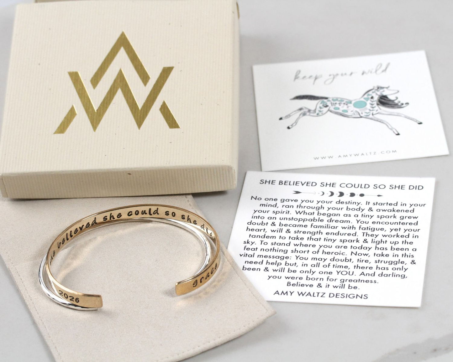 a bracelet with a motivational quote, a box with a gold logo, and a card with a message.