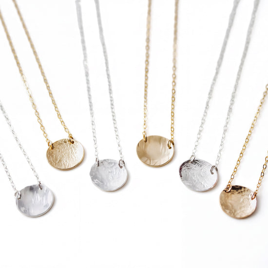 A collection of six round pendants in various colors, including gold, silver, and white, arranged in a row on a white background.
