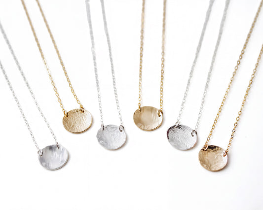A collection of six round pendants in various colors, including gold, silver, and white, arranged in a row on a white background.