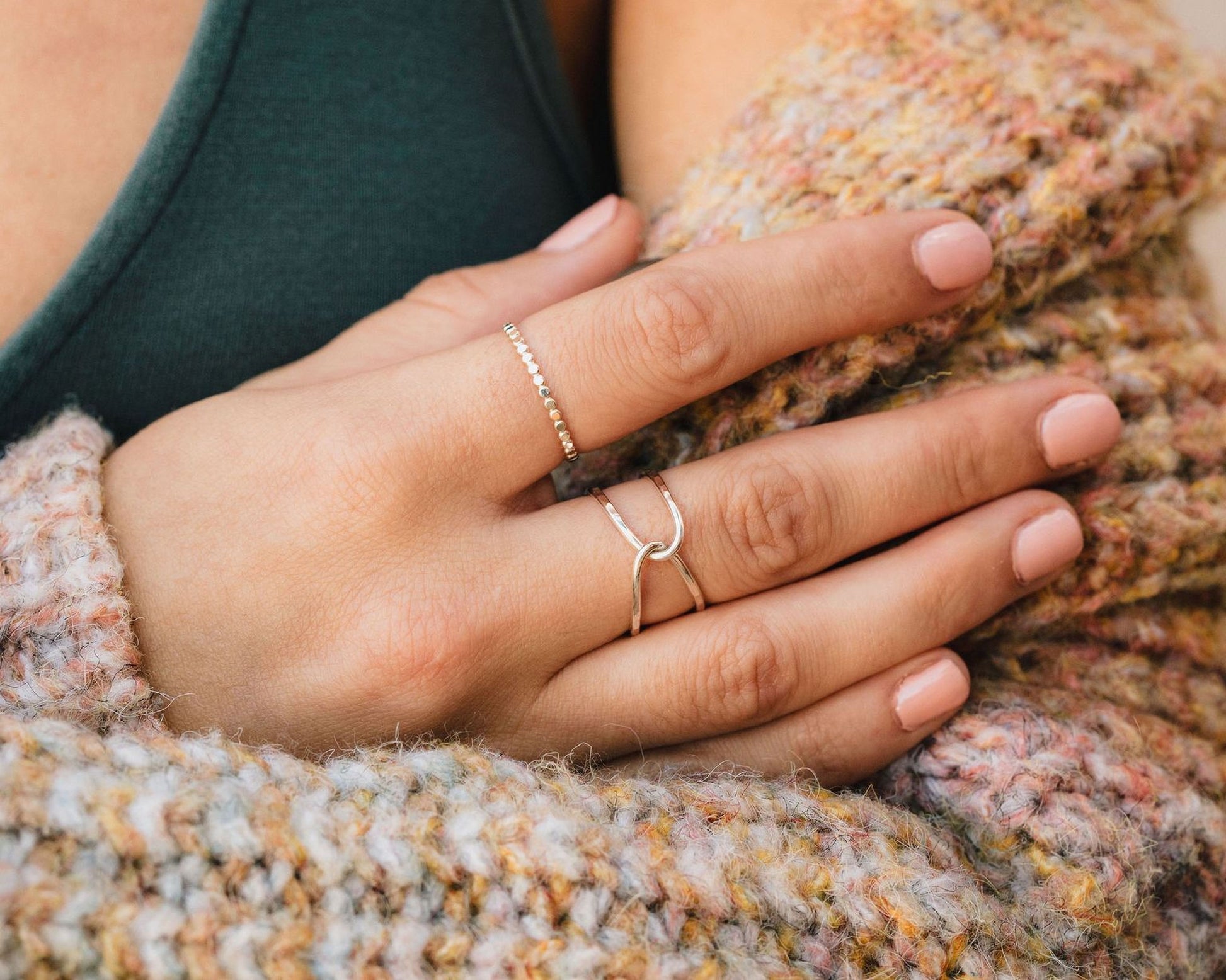 A close-up of a person's hand wearing multiple rings, including a ring on the ring finger and another ring on the index finger.