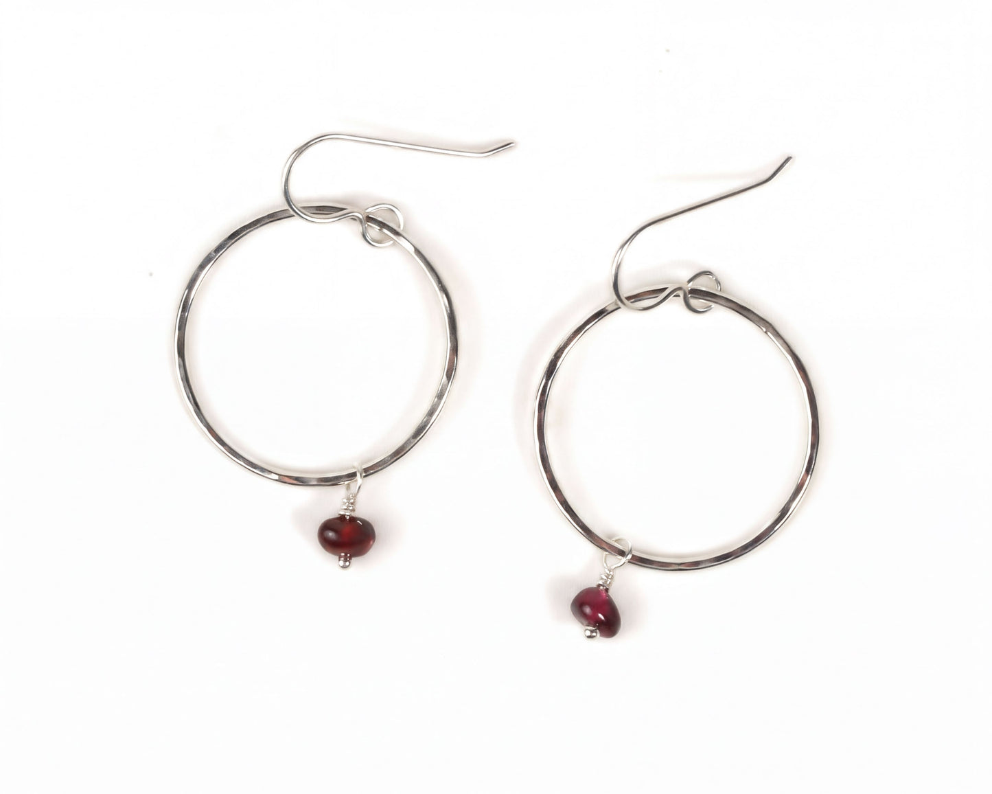 A pair of silver hoop earrings with a red gemstone hanging from each.
