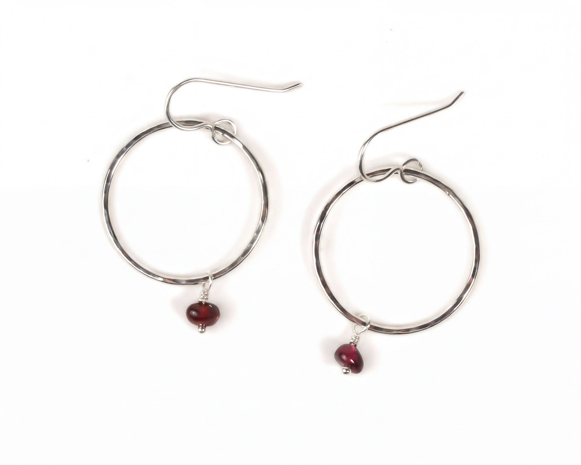 A pair of silver hoop earrings with a red gemstone hanging from each.