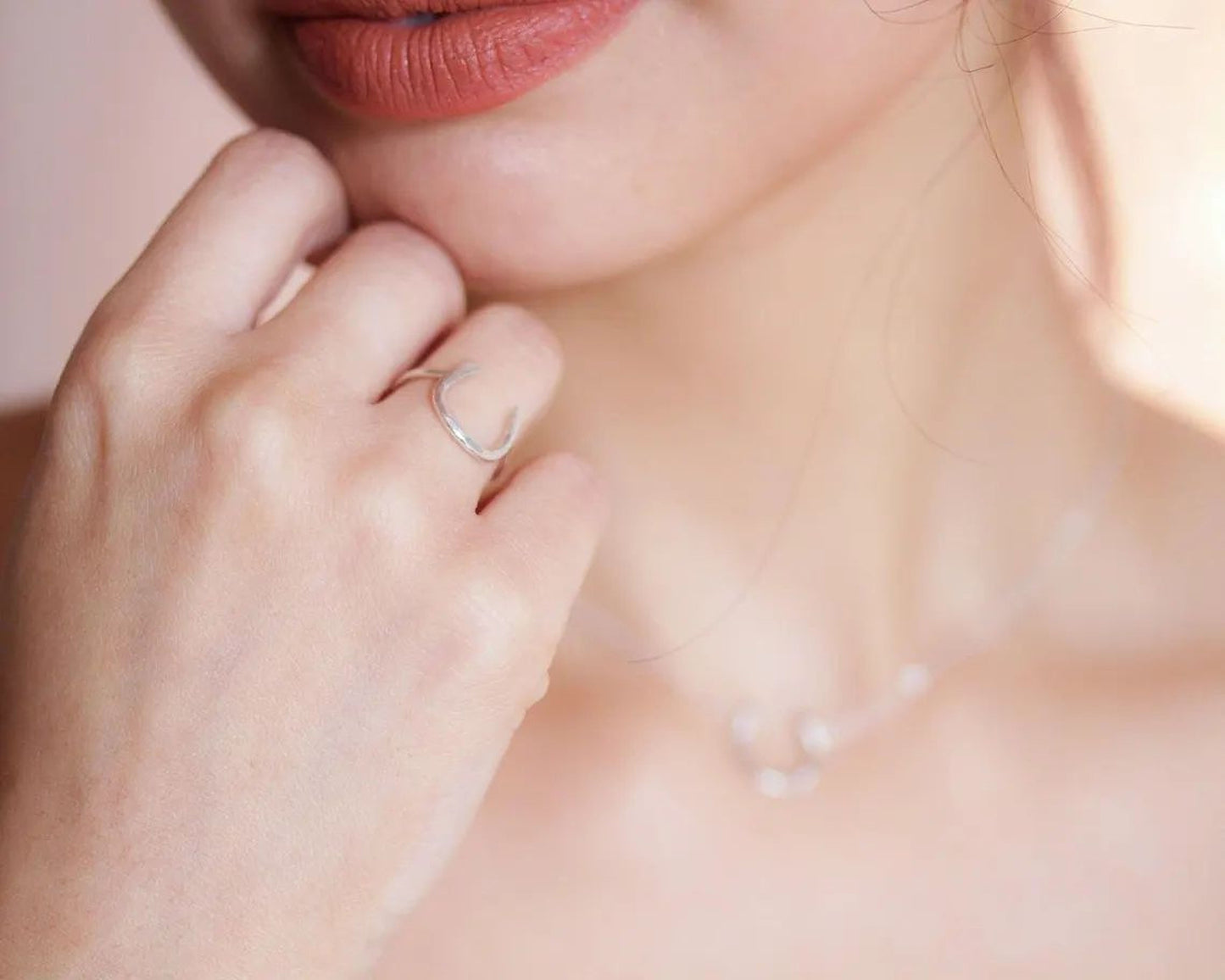 A close-up of a person's hand wearing a ring, with a necklace visible in the background.