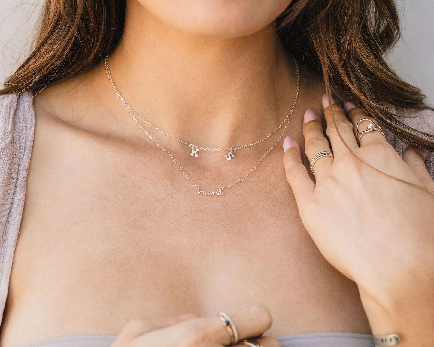 A close-up of a woman's neck and chest area, with multiple necklaces and rings visible.
