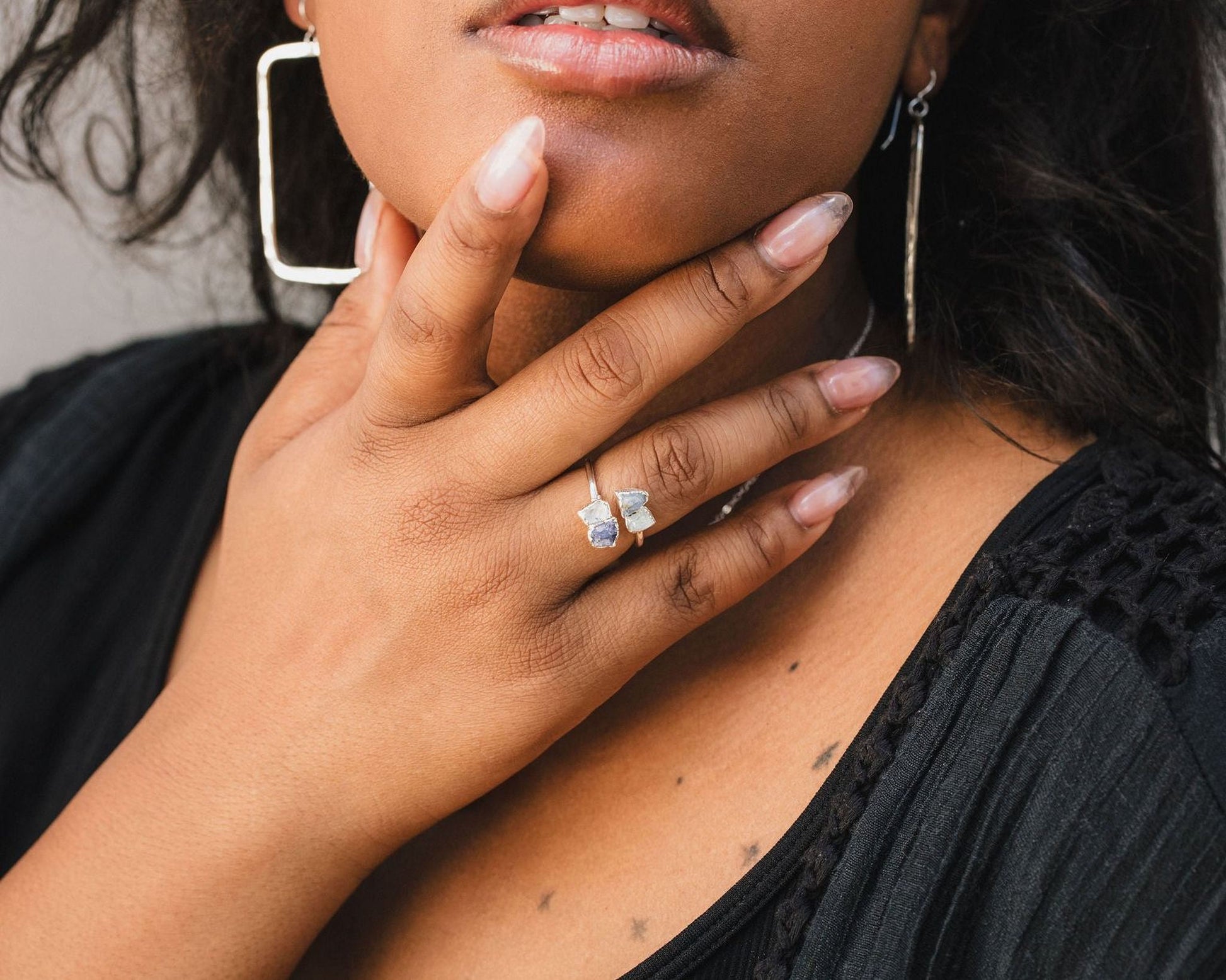 A close-up of a woman's hand wearing a ring and earrings, with her chin resting on her hand.