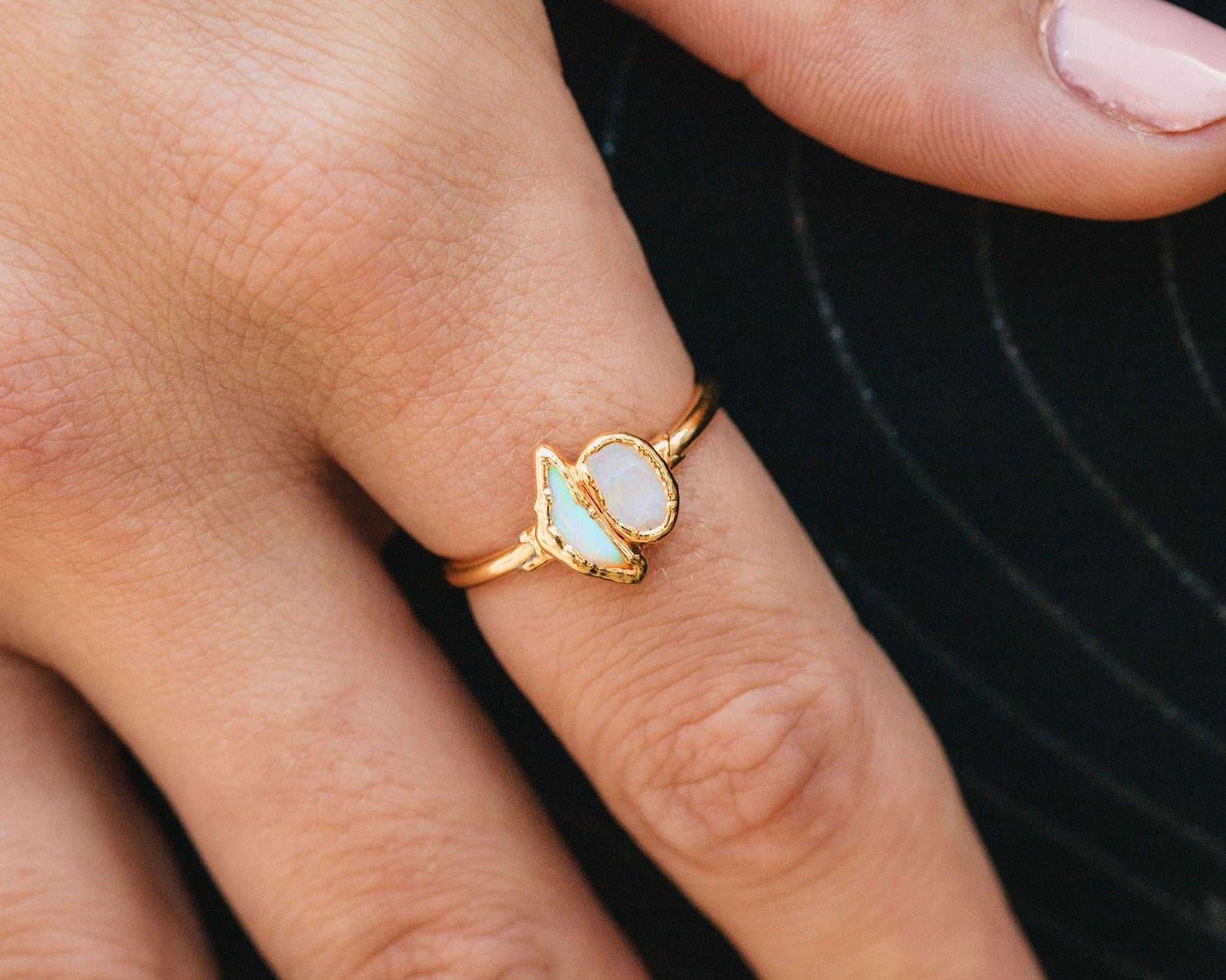A close-up of a gold ring with a single opal stone on the finger.