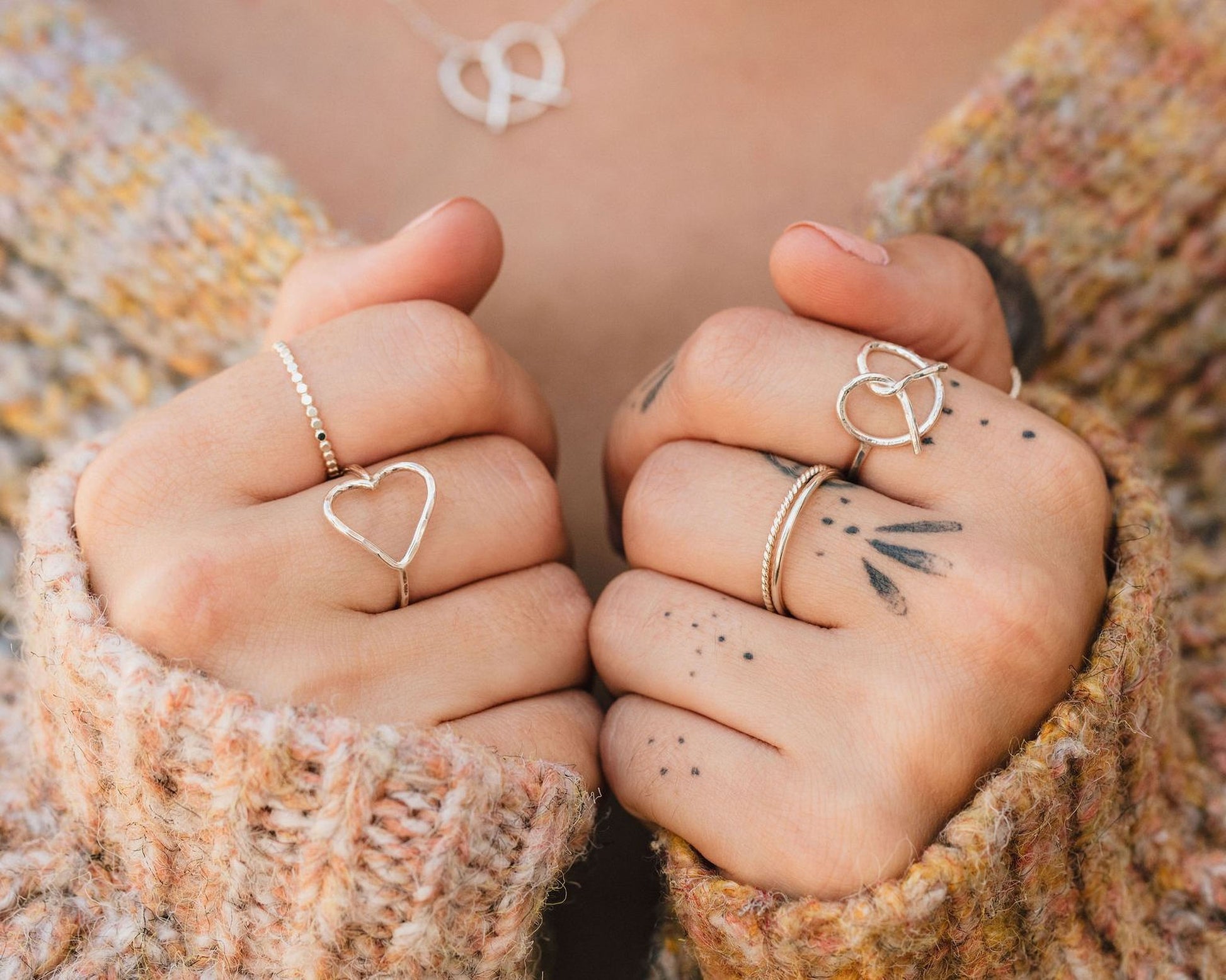 A close-up of a person's hands wearing multiple rings, including a heart-shaped ring and a ring with a peace sign symbol.
