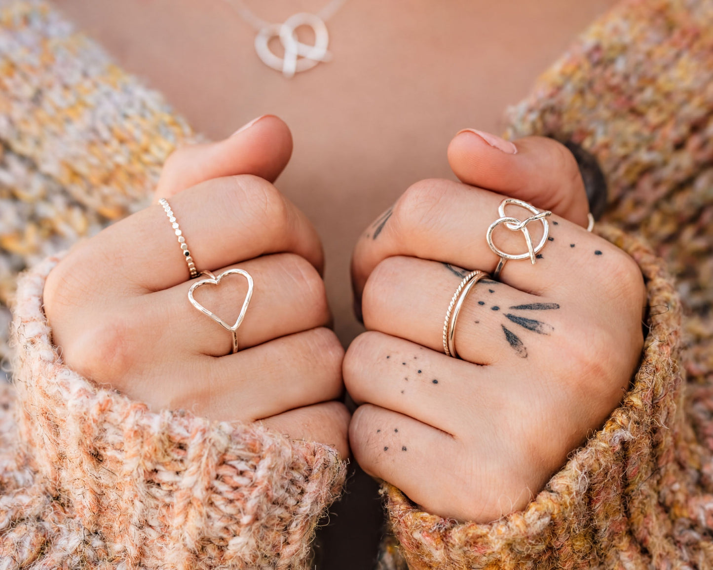 A close-up of a person's hands wearing multiple rings, including a heart-shaped ring and a ring with a peace sign symbol.