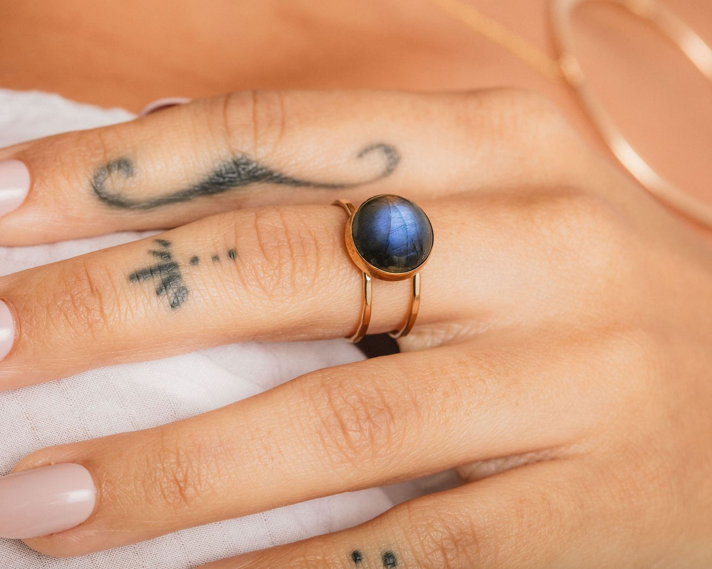 A close-up of a person's hand wearing a gold ring with a blue gemstone, and several tattoos on the fingers.