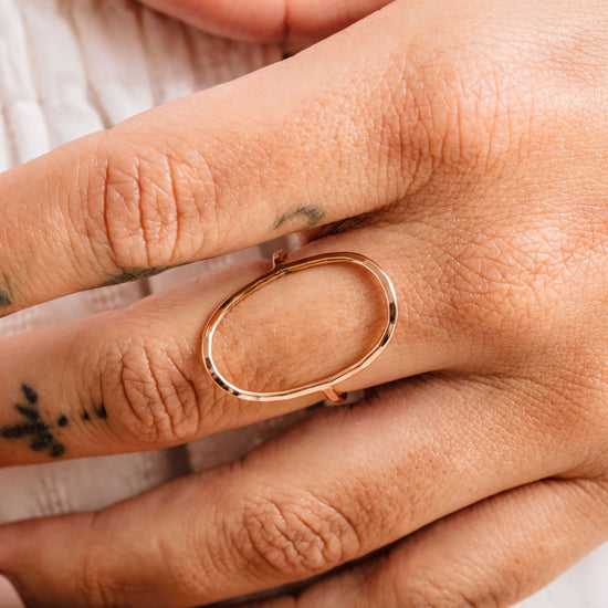 A close-up of a person's hand wearing a gold ring with an oval-shaped design.