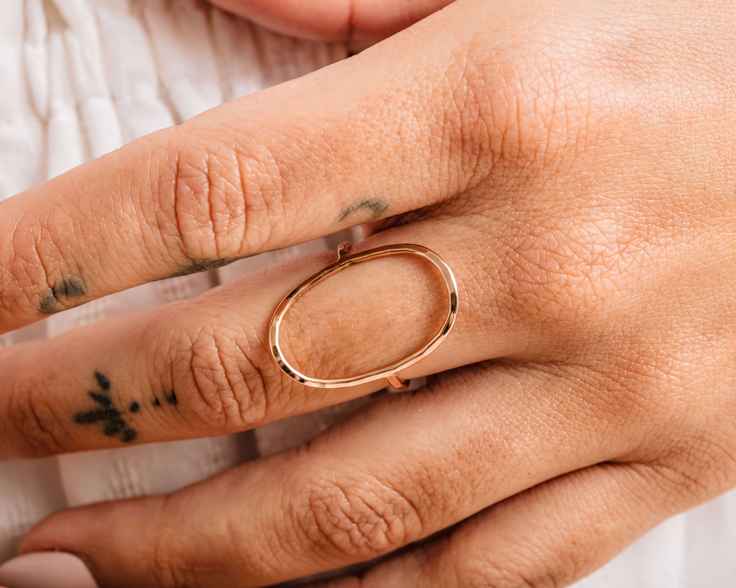 A close-up of a person's hand wearing a gold ring with an oval-shaped design.