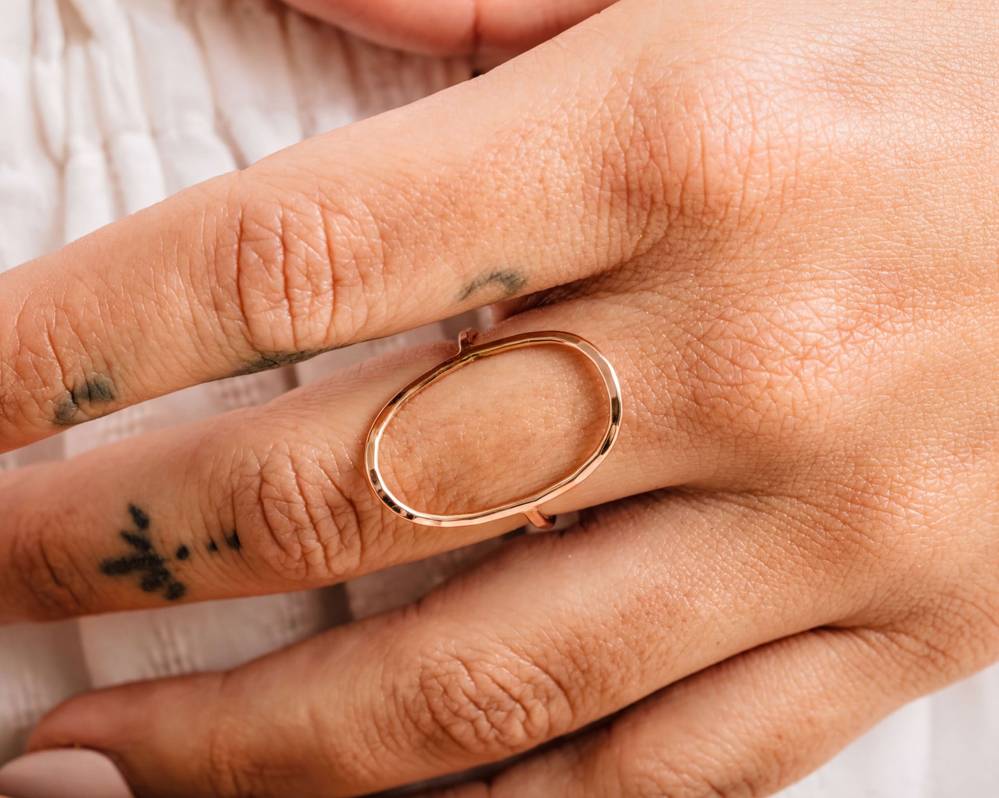 A close-up of a person's hand wearing a gold ring with an oval-shaped design.